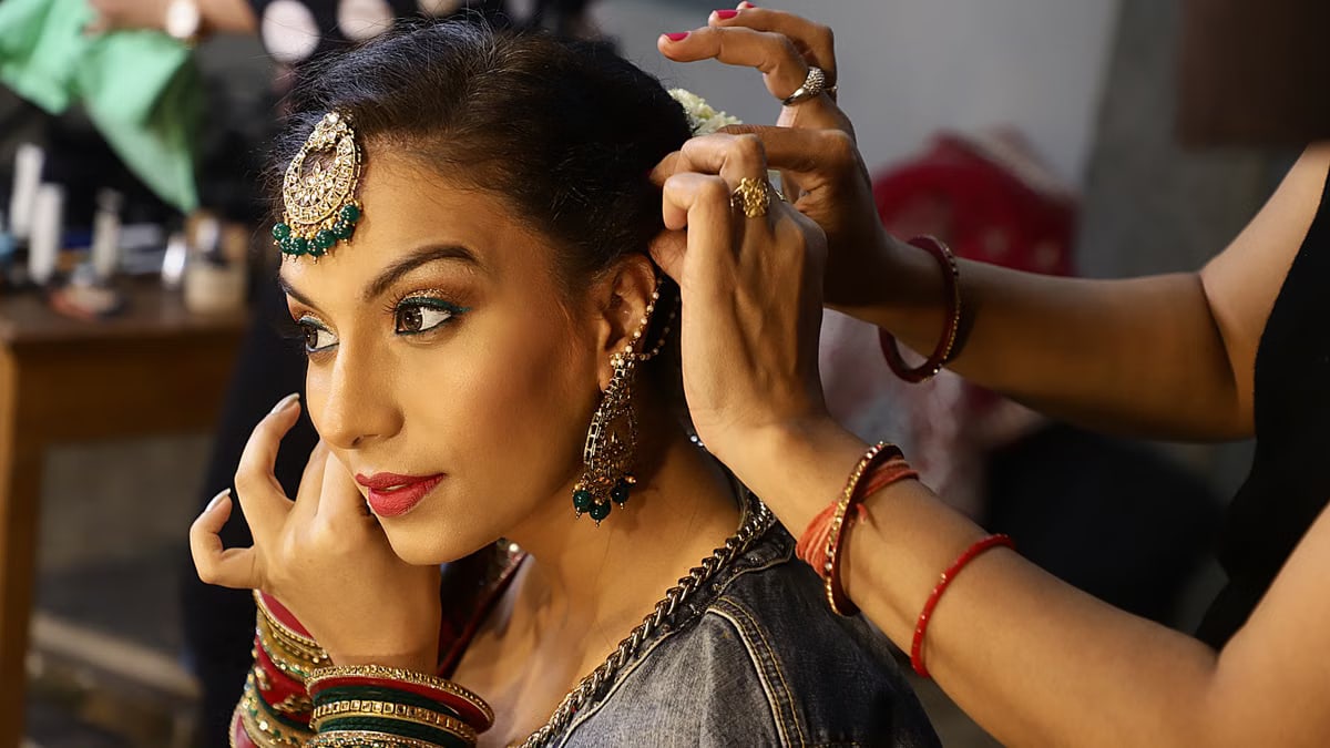 South Asian bride in traditional attire, getting ready with elegant jewelry and makeup.